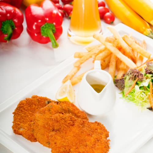 milanese style veal cutlets on a plate with fries, salad and a lemon slice
