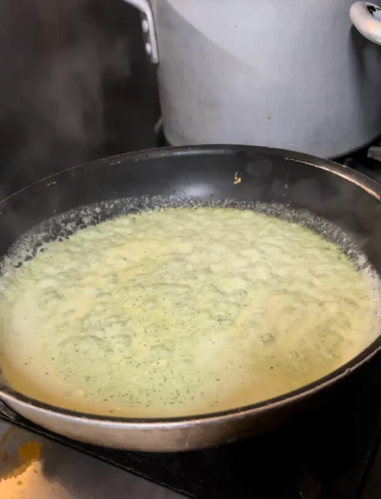 pesto cream sauce bubbling in a pan at the end of the cooking process