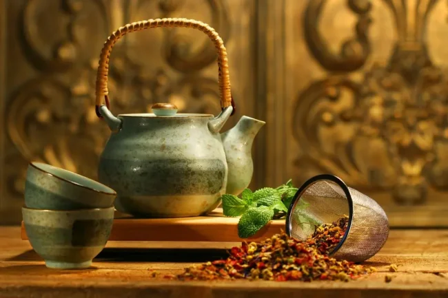 a teapot on a table next to some peppermint leaves and some loose leaf tea