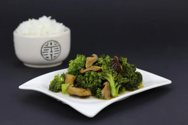 chinese broccoli on a plate next to a bowl of rice