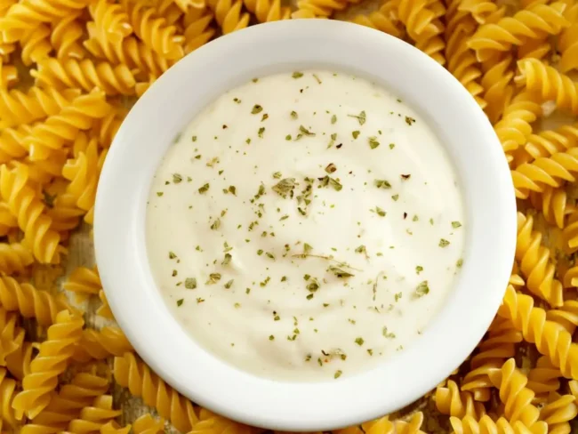 thickened alfredo sauce ina bowl above pieces of pasta