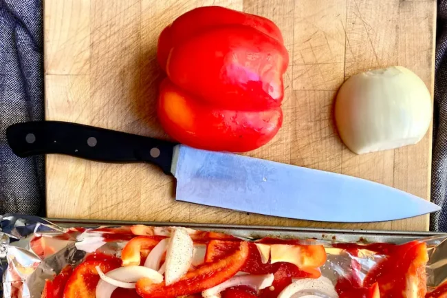 some of the ingredients for sauteed haricot verts, specifically a bell pepper and an onion, on a wooden surface next to a chef's knife