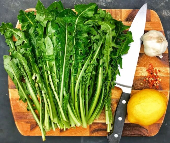 a wooden plate with the ingredients for dandelion greens and a knife