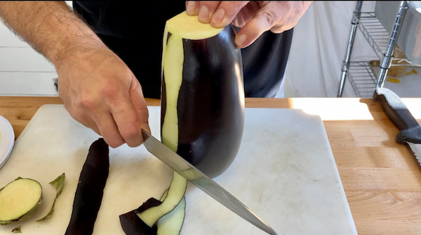 a hand peeling an eggplant with a knife