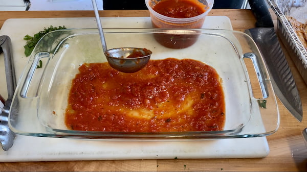 a baking dish with a layer of tomato sauce on the bottom
