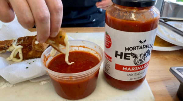 a hand dumping a mozzarella stick in a bowl of marinara sauce