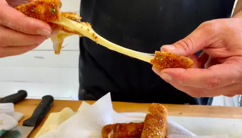 hands pulling two pieces of mozzarella stick before dipping them in marinara sauce