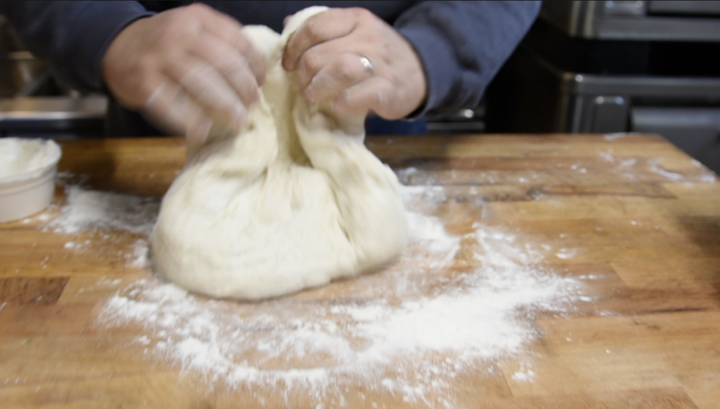 hands grabbing and folding a freshly made roman pizza dough