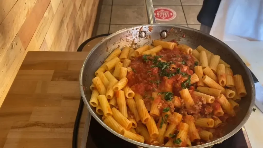 a saucepan full of rigatoni dressed with bolognese sauce
