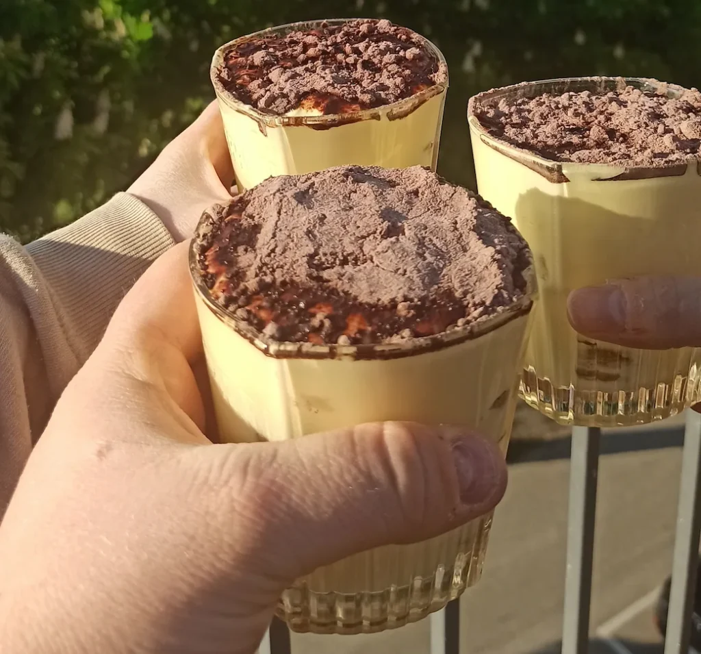 3 hands holding individual tiramisu cups in the open air