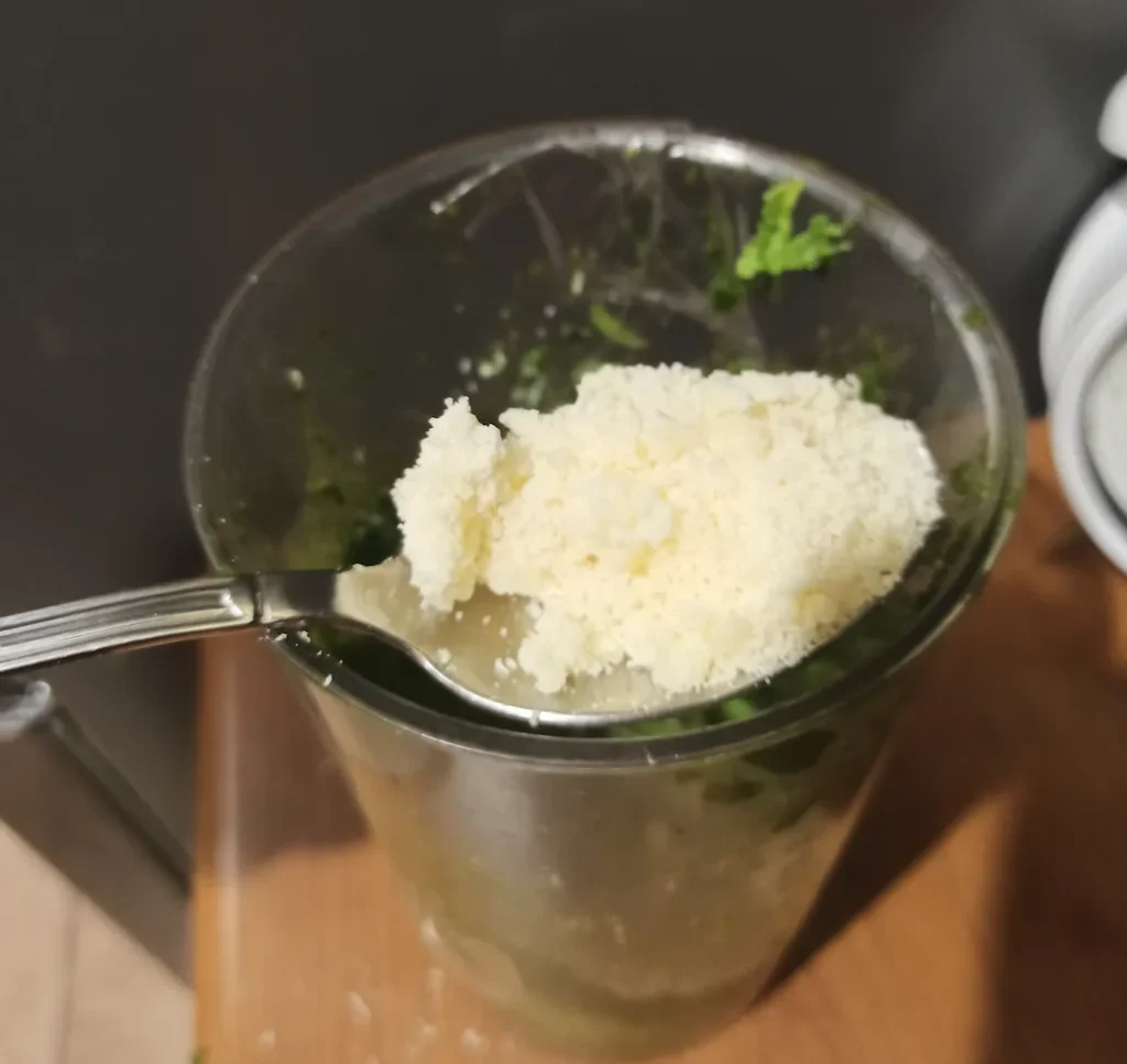 adding grated cheese to the pesto