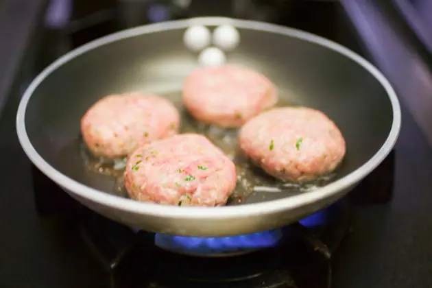 4 frozen burgers cooking on a stove