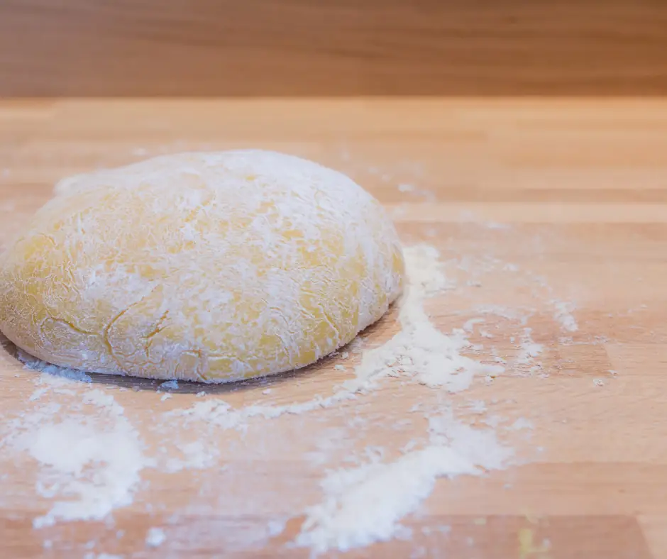 an egg pasta dough ball on a floured surface