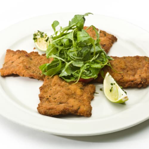 breaded veal cutlets with lemon and fresh salad leaves