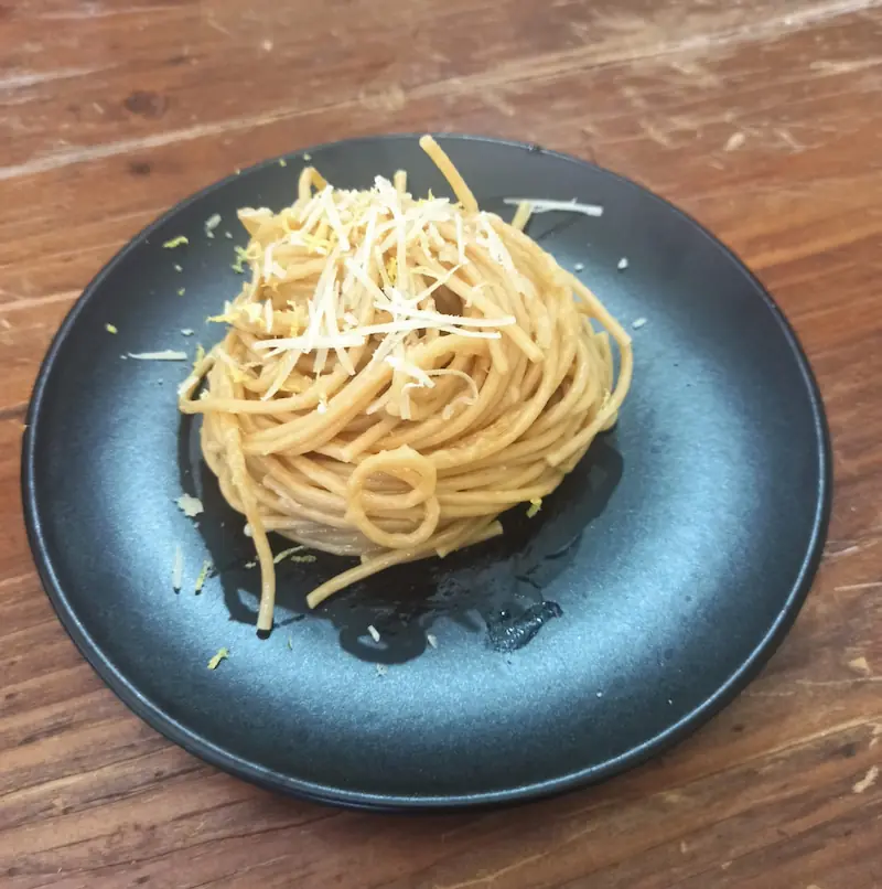 a black plate with freshly made lemon pasta on top of it