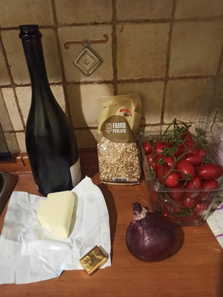 some of the ingredients for this farro risotto recipe: an onion, date tomatoes, butter, farro and white wine