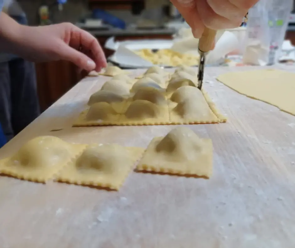 a hand using a pasta cutter to cut out some freshly made ravioli
