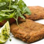 italian veal cutlets aside with some salad and a lemon slice