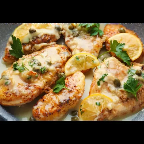 a picture of chicken piccata with lemon slices and fresh green herbs