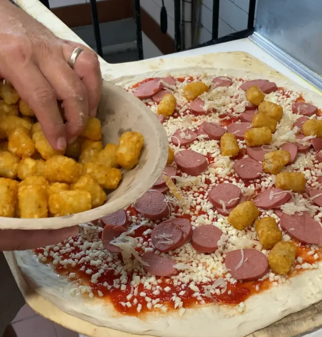 a hand adding tater tots to german pizza
