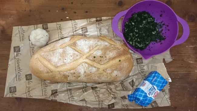 the ingredients for this garlic ciabatta bread recipe on a table: one loaf of ciabatta bread, some garlic, fresh herbs, and butter.