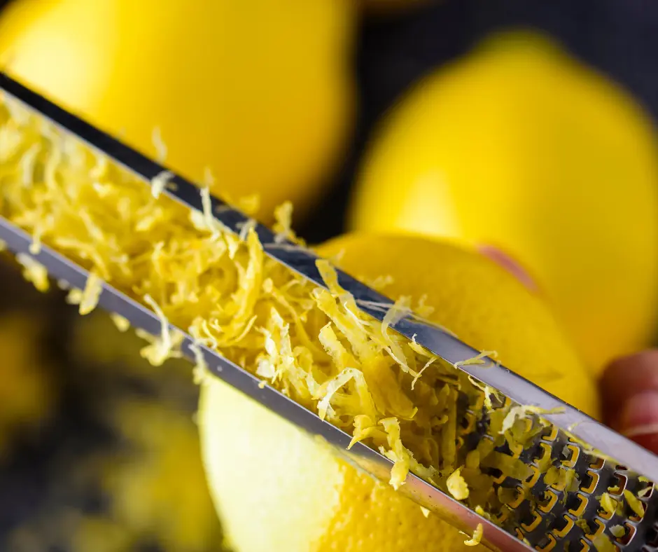 some grated lemon zest still attached to the zester, with some lemons in the background