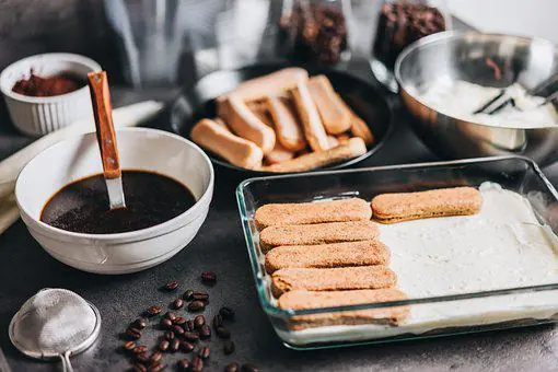 a baking dish with a layer of soaked savoiardi biscuits, next to a bowl full of coffee