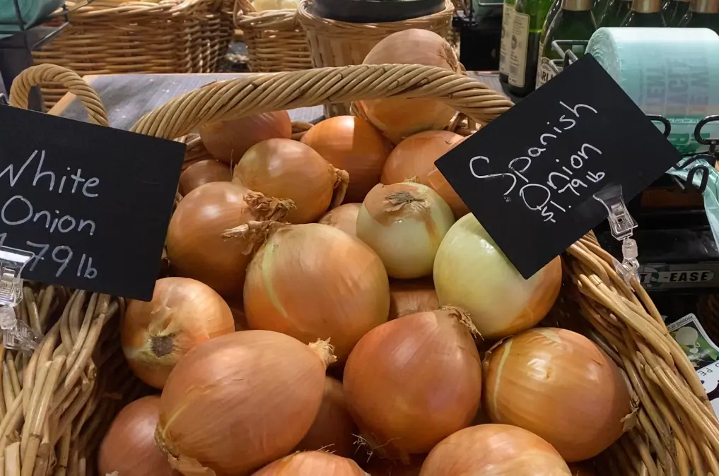 a bunch of Spanish onions in a basket at a grocery store with price tags