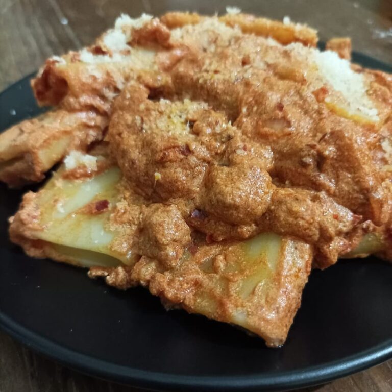 a black plate full of paccheri pasta with a dressing made of ricotta, 'nduja, and tomato sauce, garnished with some grated parmesan cheese