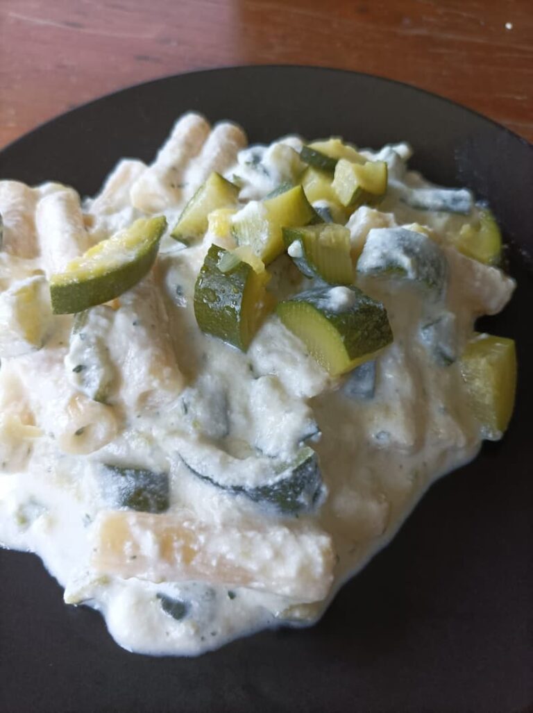 a small portion of penne pasta with ricotta and zucchini on a black plate