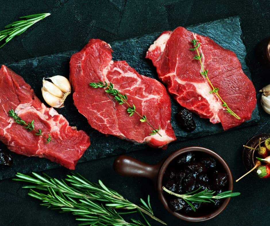 three pieces of raw steak with herbs, garlic and olives