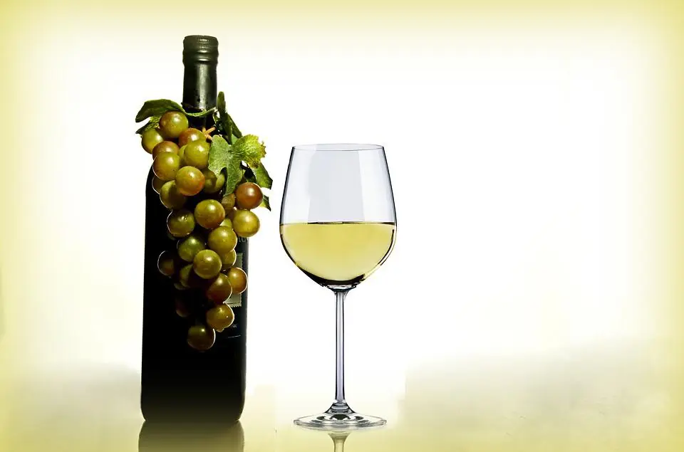 a glass of white wine next to a bottle decorated with grapes