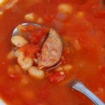 a spoon dipping into a white bean and sausage soup