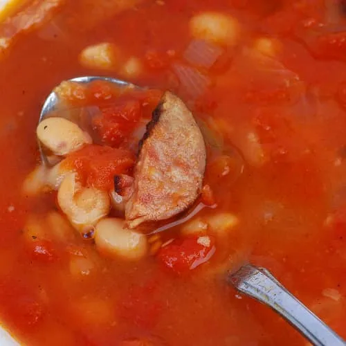 a spoon dipping into a white bean and sausage soup