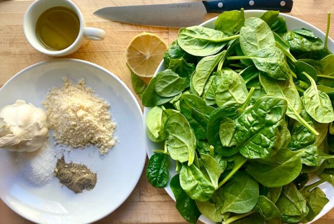 the ingredients for italian sauteed spinach on a wooden surface with a chef's knife