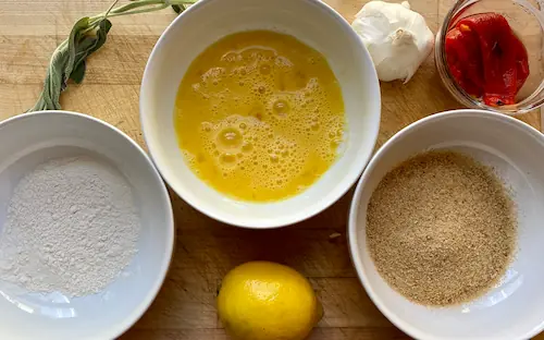 a simple breading station with three bowl: one with flour, one with beaten eggs, and one with breadcrumbs