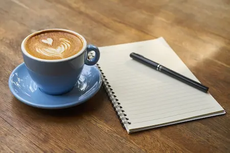a cup of cappuccino next to a notebook on a table