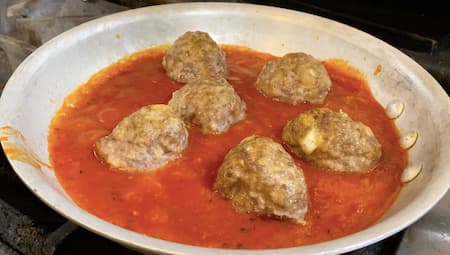 cooking frozen meatballs on a stove in tomato sauce