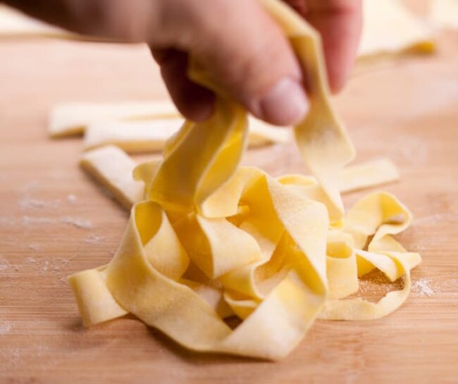 a hand holding fresh egg pasta noodles