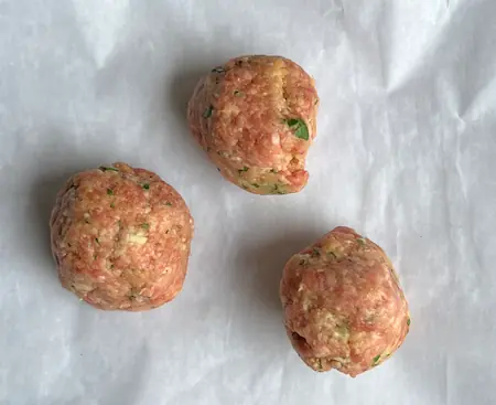 three raw meatballs ready to be fried