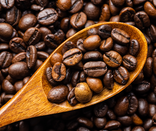 a mix of arabica and robusta beans on a wooden spoon, with other beans in the background. 