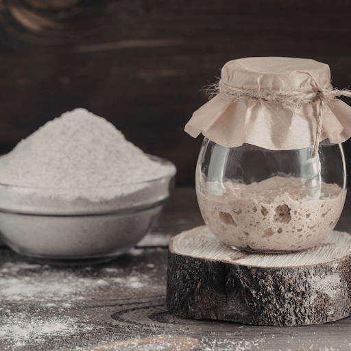 Jar of sourdough starter beside bowl of flour